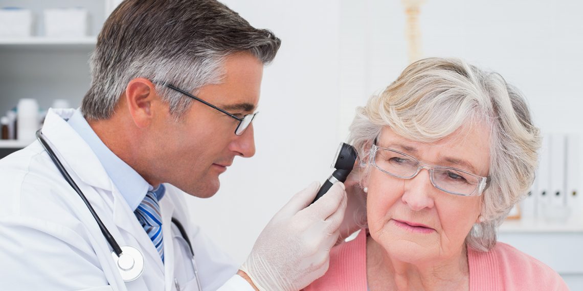 Doctor examining female patients ear with otoscope in clinic