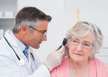 Doctor examining female patients ear with otoscope in clinic