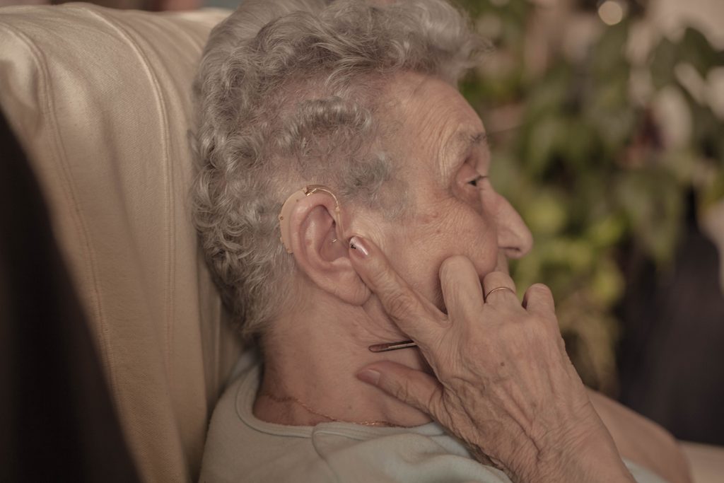 Old woman showing with her finger on hearing aid.