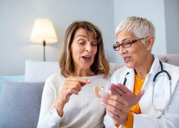 The doctor laryngologist explains senior woman how to wear a hearing aid. Mature female doctor hearing specialist in her office Showing Hearing Aid To female Patient In Clinic
